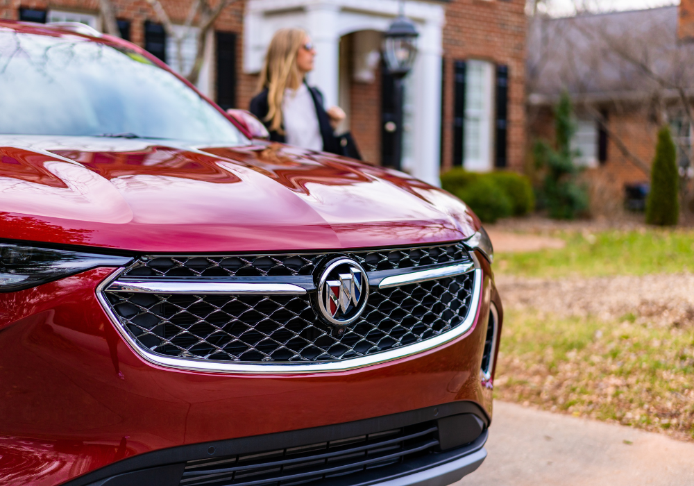 Close up of the front of a red Buick SUV with a woman in the background